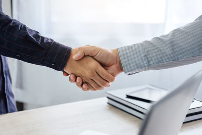 Midsection of colleagues handshaking above desk in office