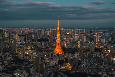 Illuminated buildings in city against cloudy sky