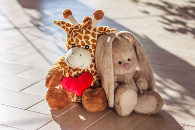 Children's soft plush toy giraffe and bunny sit on wooden background, hard light and shadow