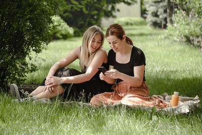 Two woman having fun on picnic. friends on blanket communicating happily making selfie. cheerfully