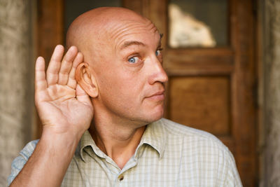 Close-up bald man holds his hand to his ear pretending to overhear. emotional