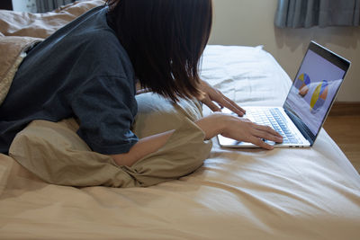 Midsection of woman using laptop on bed at home