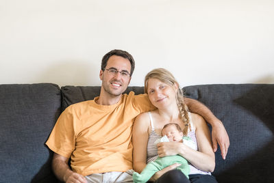 Portrait of smiling mother and father with son sitting on sofa at home