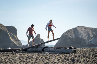 Teenage couple balancing on driftwood see-saw on beach