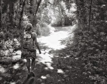 Rear view of mature woman with backpack walking on road amidst trees in forest