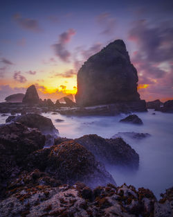 Rocks on sea shore against sky during sunset