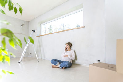 Young woman using phone while sitting on wall