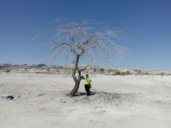 Man standing on bare tree against clear sky