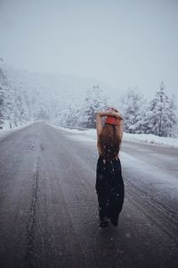 Rear view of person photographing on snow covered road