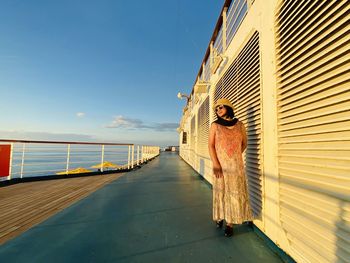 Woman standing on railing by sea against sky