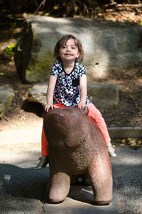 Portrait of smiling girl sitting on animal representation in playground