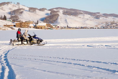 The snowmobile with unidentified fishermen is riding along the snowy lake in the winter. 