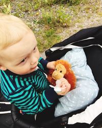 High angle view of toddler boy playing with toy monkey while sitting on baby carriage