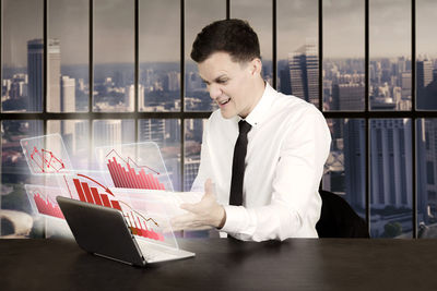 Digital composite image of happy businessman using laptop with graph icons in office