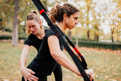 Happy friends exercising with straps while standing by tree