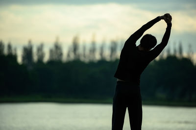 Close-up of silhouette hand against lake during sunset