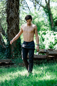 Full length of shirtless young man standing on grass