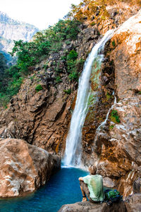 Rear view of man sitting against waterfall