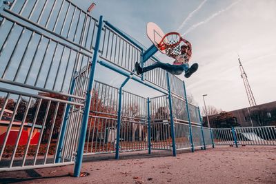 Low angle view of man hanging on basketball hoop against sky