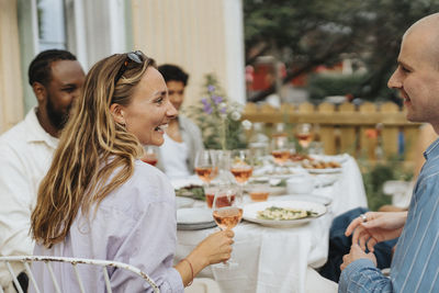 Happy young woman holding wineglass while laughing with male friend during dinner party at cafe