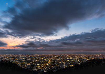 Aerial view of illuminated cityscape against cloudy sky during sunset