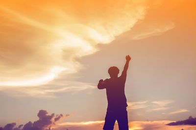 Silhouette man with arms raised standing against sky during sunset