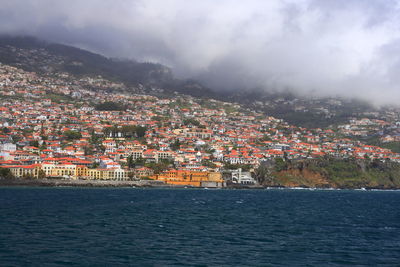 Aerial view of townscape by sea against sky