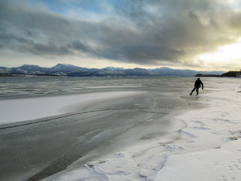 Man on snowy land against cloudy sky at sunset