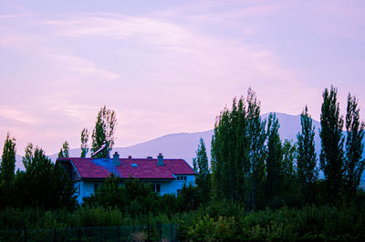 Built structure by trees and houses against sky at sunset