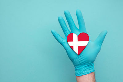 Close-up of hand holding heart shape against blue background