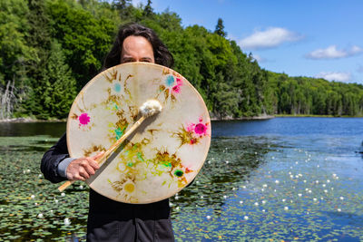 Rear view of woman standing by lake against trees