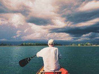 Man rowing boat in lake against cloudy sky during sunset