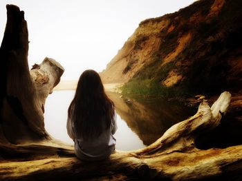 Rear view of woman sitting on rock formation against clear sky