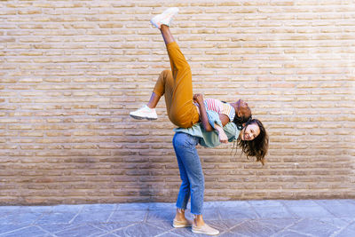 Cheerful woman carrying friend on back by wall