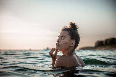 Shirtless young woman swimming in sea against sky