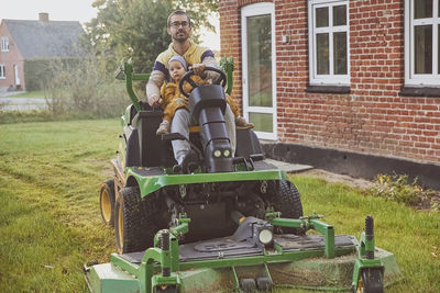 Man with a little daughter mows the lawn near the house in autumn