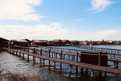 Pier over river by houses against sky