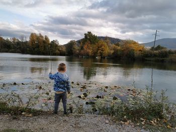 Rear view of man standing by lake against sky