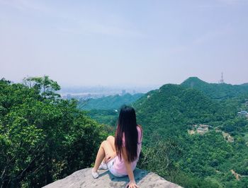 Rear view of woman sitting on mountain against clear sky