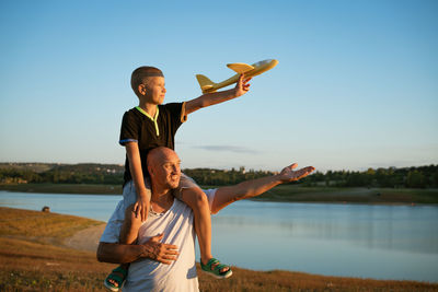 Father holding son on shoulders at sunset with airplane in hand