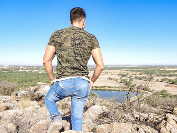 Rear view of man standing on rocks against clear blue sky