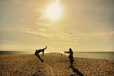 Silhouette people on beach against sky during sunset