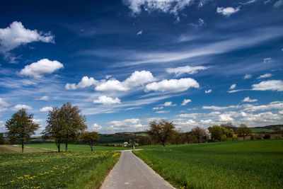 Empty road amidst field against sky