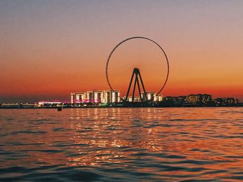 Ferris wheel by sea against sky during sunset