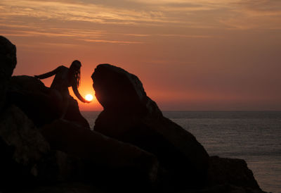 Silhouette rocks by sea against sky during sunset