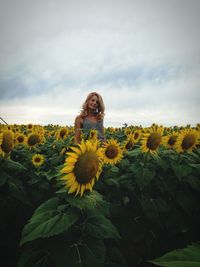 Portrait of woman standing in sunflower field against sky