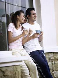 Smiling couple talking while having coffee against wall