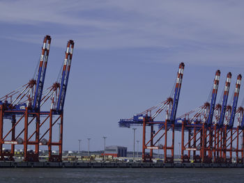 Cranes at harbor against sky