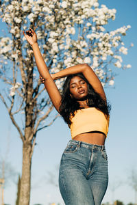 Low angle view of woman standing by tree against sky