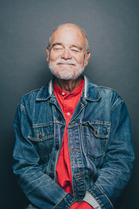 Smiling senior man with eyes closed standing against gray background
